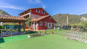 Una casa roja de dos pisos con techo de tejas, terraza de madera y césped cuidado.