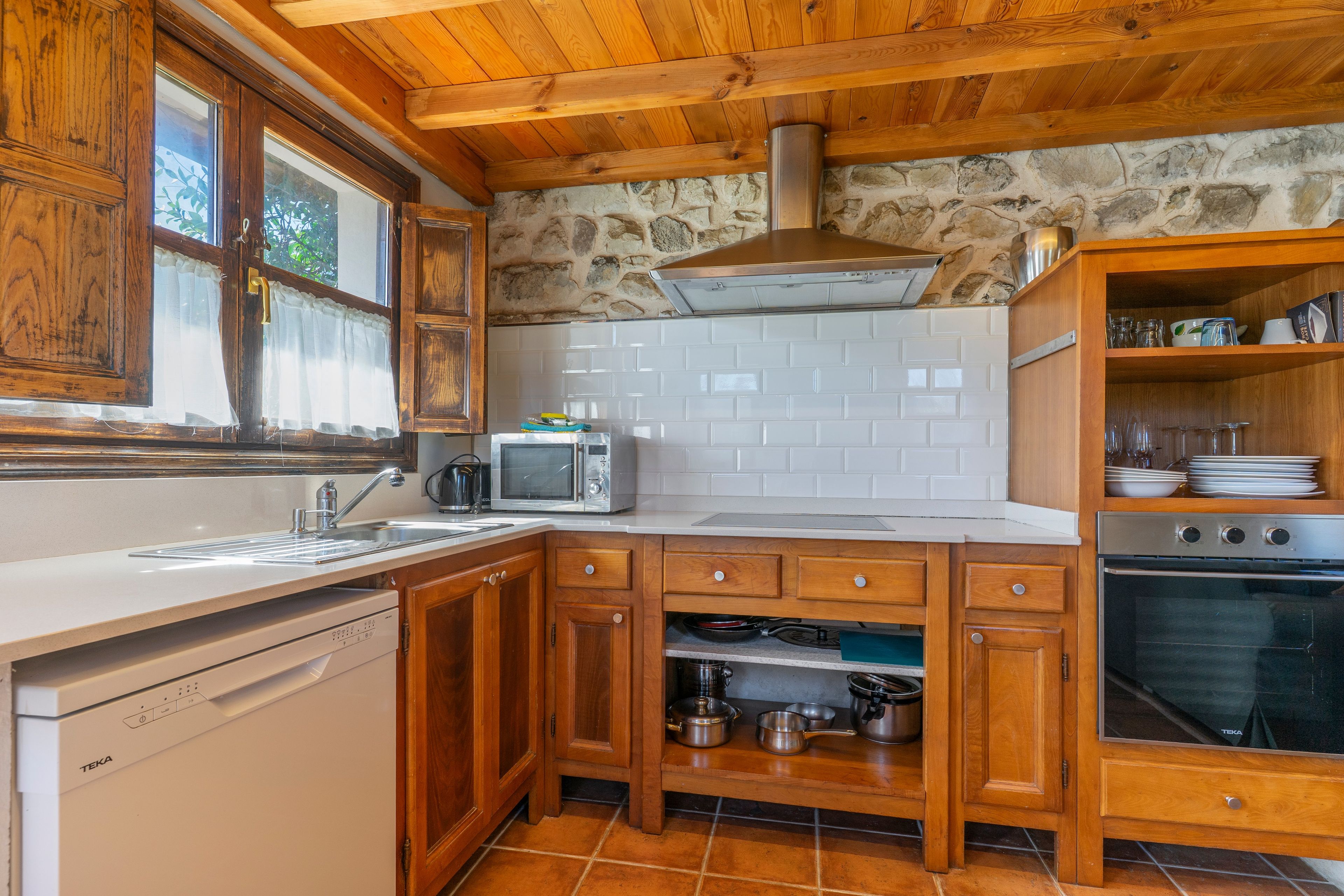 Una cocina con armarios de madera, horno empotrado, microondas y lavavajillas.