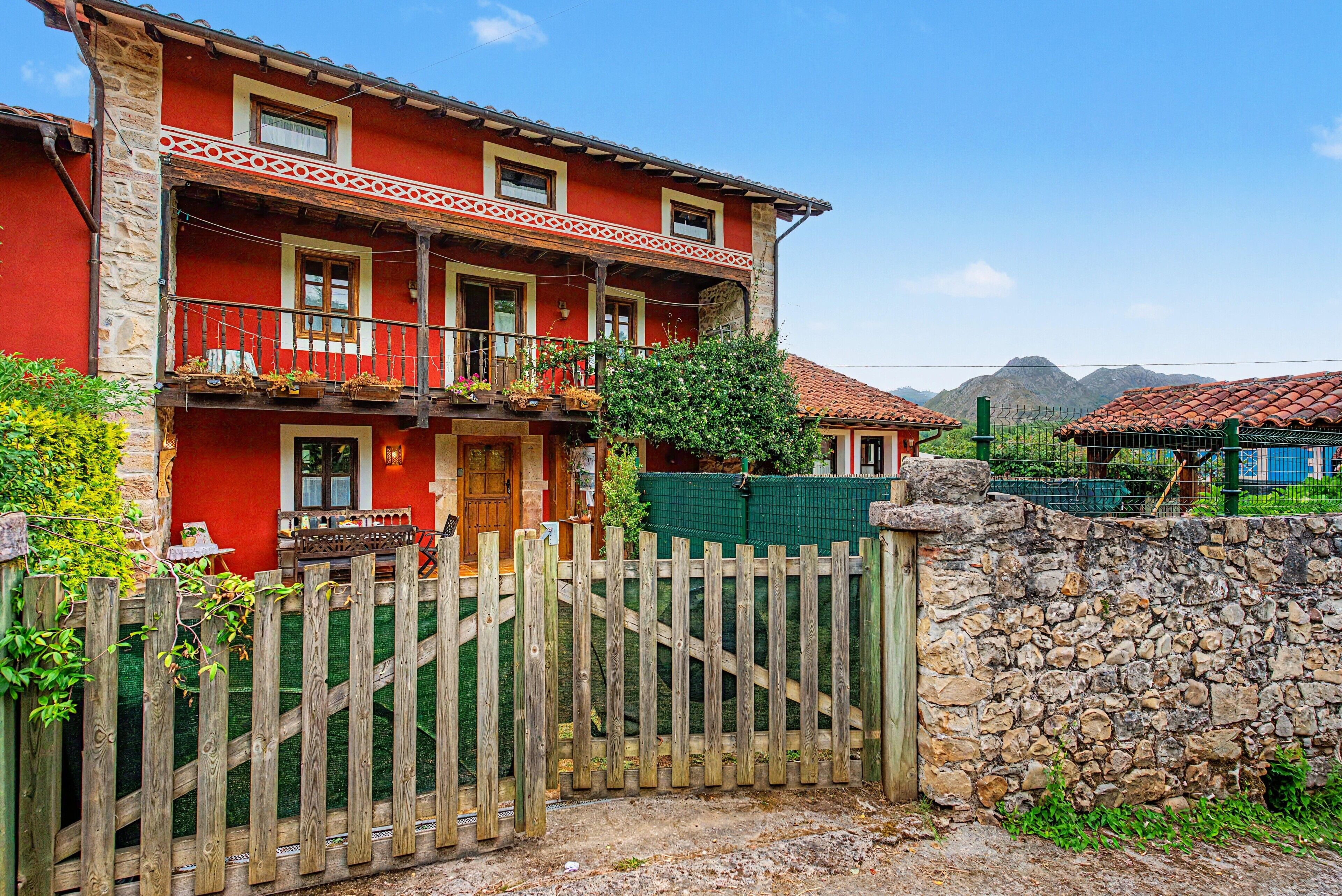 Un edificio rojo de dos pisos con un balcón de madera, una pared de piedra y una cerca de madera.