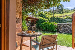 Un patio con una mesa redonda, una silla y una pequeña zona ajardinada con un muro de piedra y vegetación.
