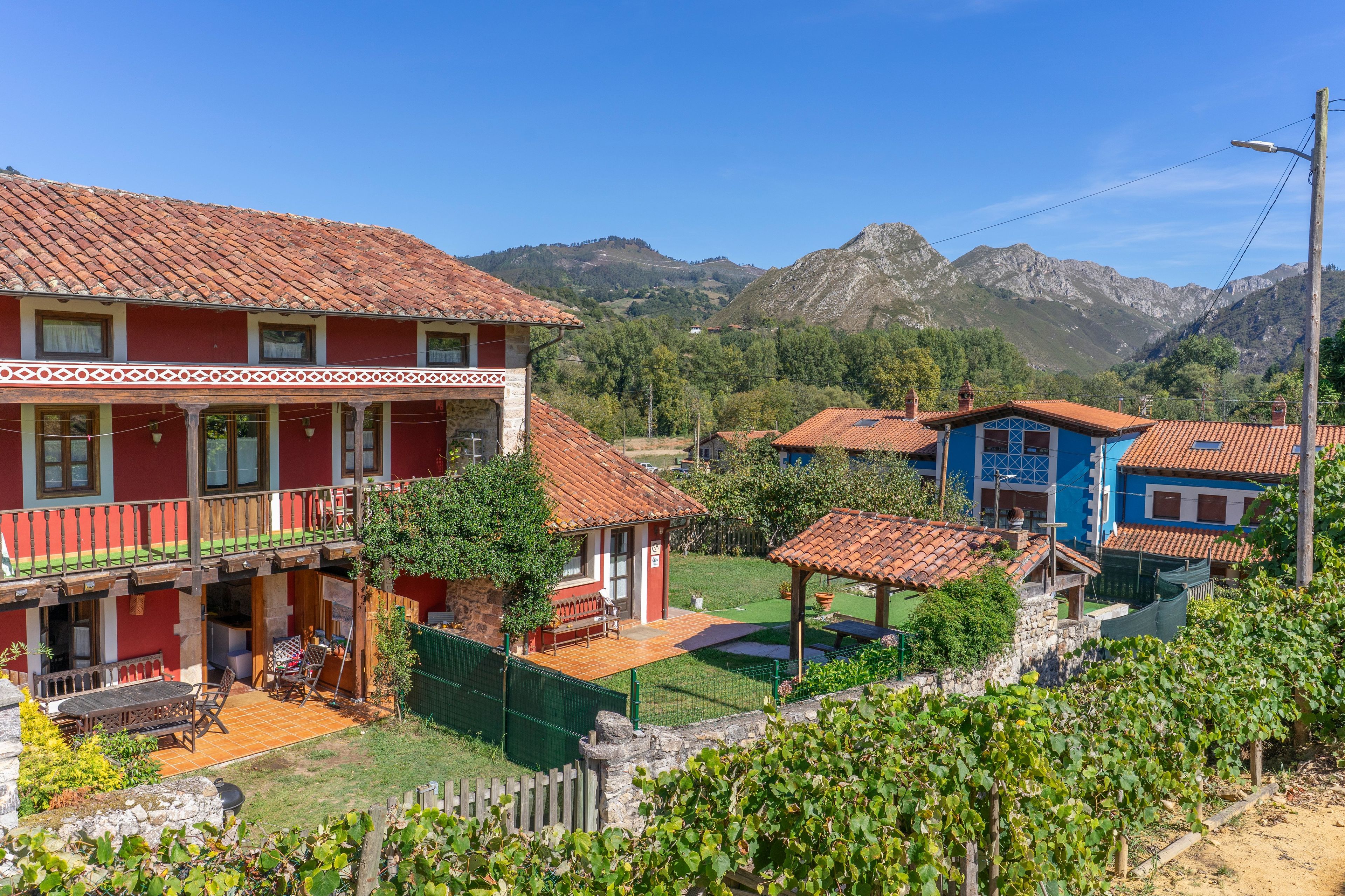 A red building with a balcony and a blue building with a tiled roof in a rural setting with mountains in the background.