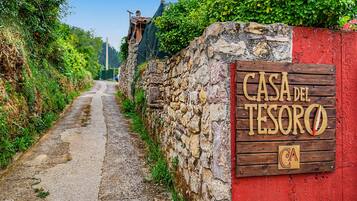 Una pared de piedra rústica con un letrero de madera que dice 'CASA DEL TESORO' y un estrecho sendero de tierra que se adentra en la distancia.