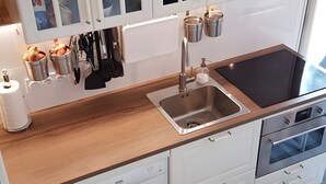 Moderni keittiö, jossa on valkoiset kaapit, ruostumattomasta teräksestä valmistettu allas ja sisäänrakennettu uuni.