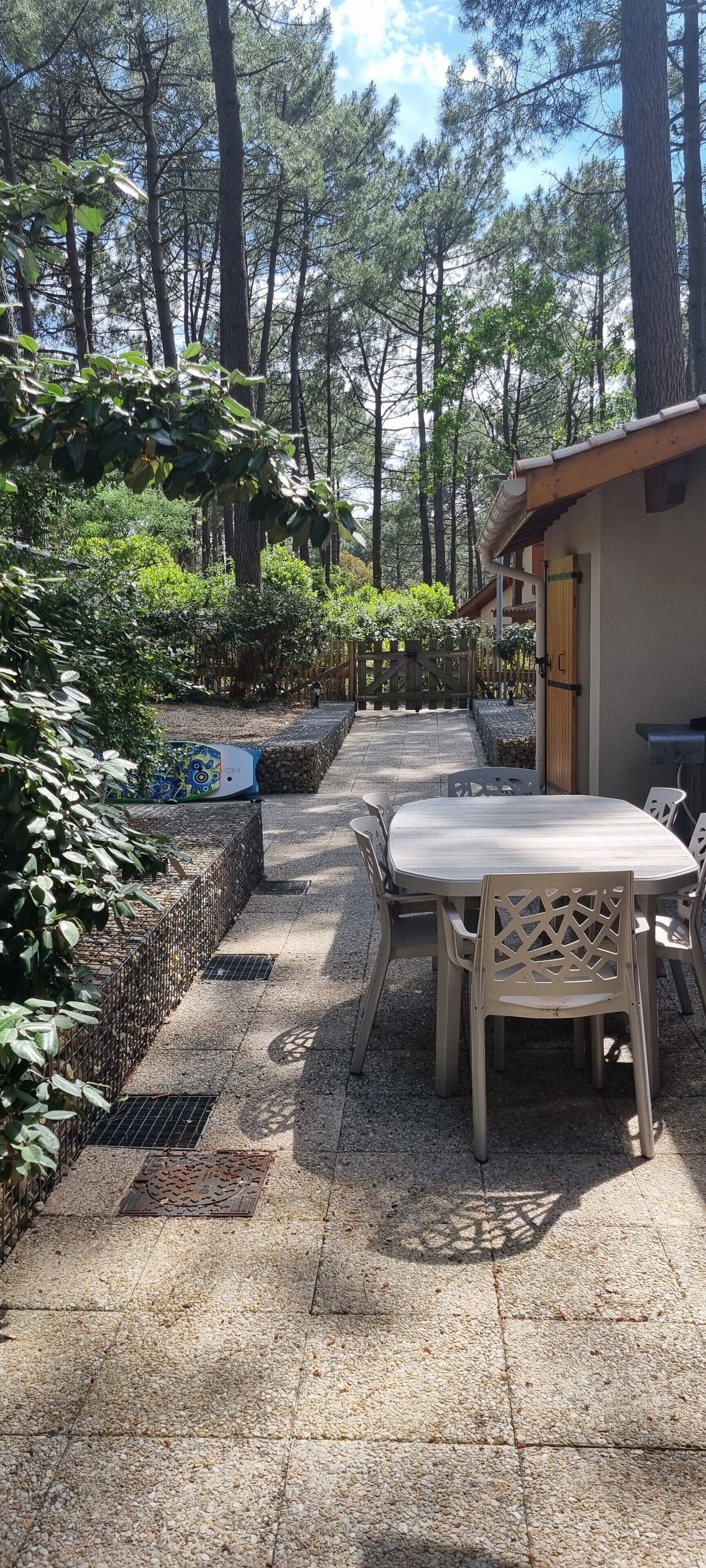 Ein möblierter Terrassenbereich mit Tisch und Stühlen, umgeben von einem Garten mit verschiedenen Pflanzen und Bäumen.