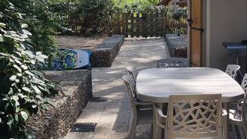 Ein möblierter Terrassenbereich mit Tisch und Stühlen, umgeben von einem Garten mit verschiedenen Pflanzen und Bäumen.