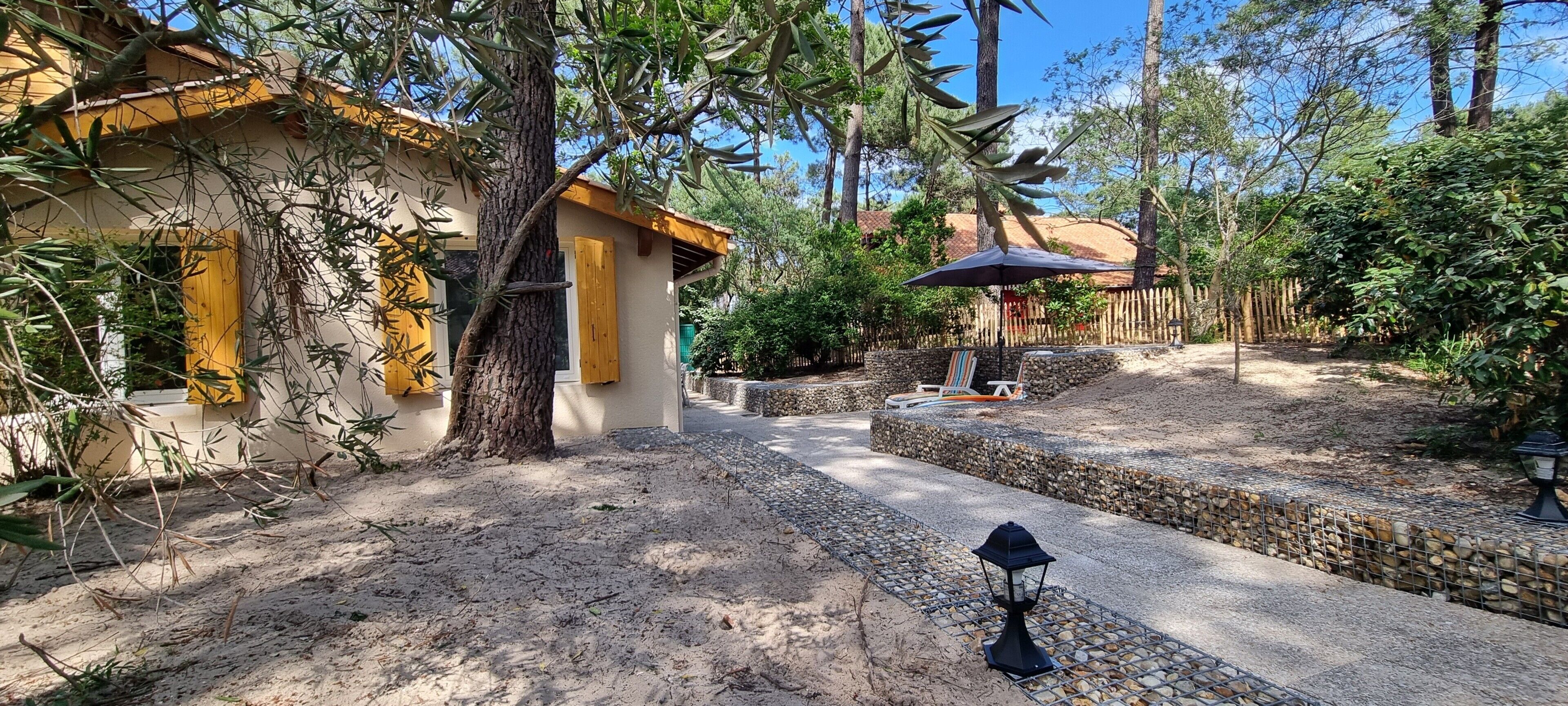Une cour avec un chemin en pierre, une clôture en bois et un espace de repos couvert, agrémenté d’un parasol.