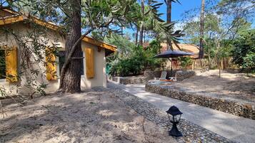 Une cour avec un chemin en pierre, une clôture en bois et un espace de repos couvert, agrémenté d’un parasol.