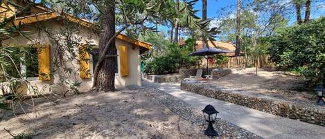 A courtyard with a stone pathway, a wooden fence, and a covered seating area with an umbrella.