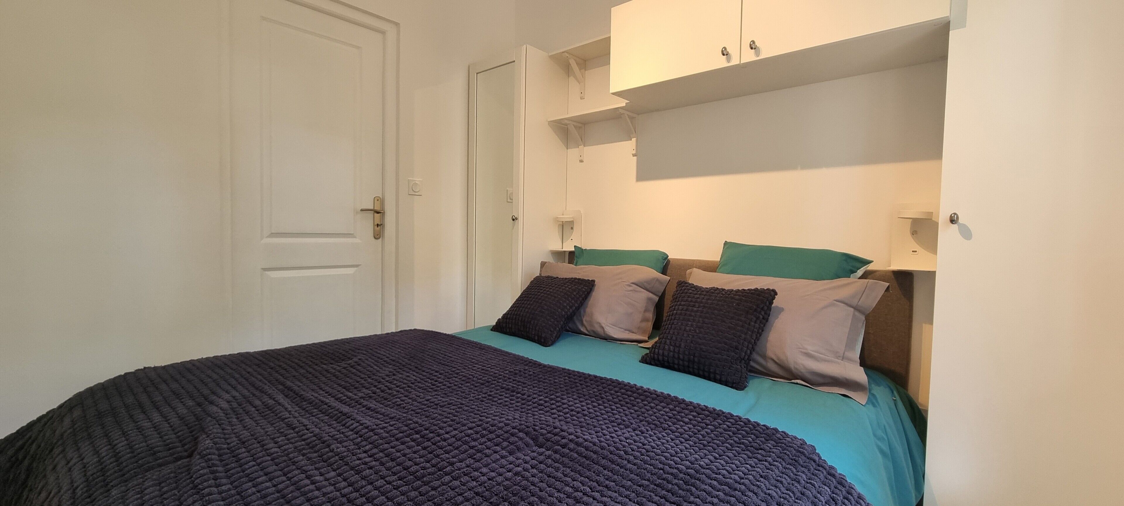 Une chambre à coucher avec un lit, des oreillers, une porte et une armoire blanche.