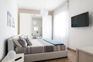 A modern bedroom with a bed, a bedside table, a TV mounted on the wall, and a bathroom visible through an open door. - Fly by Suites Pescara (Pescara)