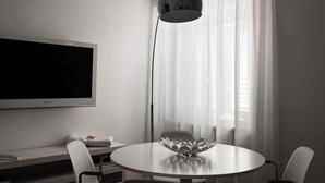 A modern room with a flat-screen TV, a round table with chairs, a decorative bowl, and sheer curtains. - Fly by Suites Pescara (Pescara)