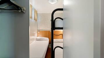 Una habitación de hotel compacta con literas, un escritorio pequeño y un perchero.