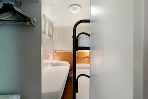Una habitación de hotel compacta con literas, un escritorio pequeño y un perchero.
