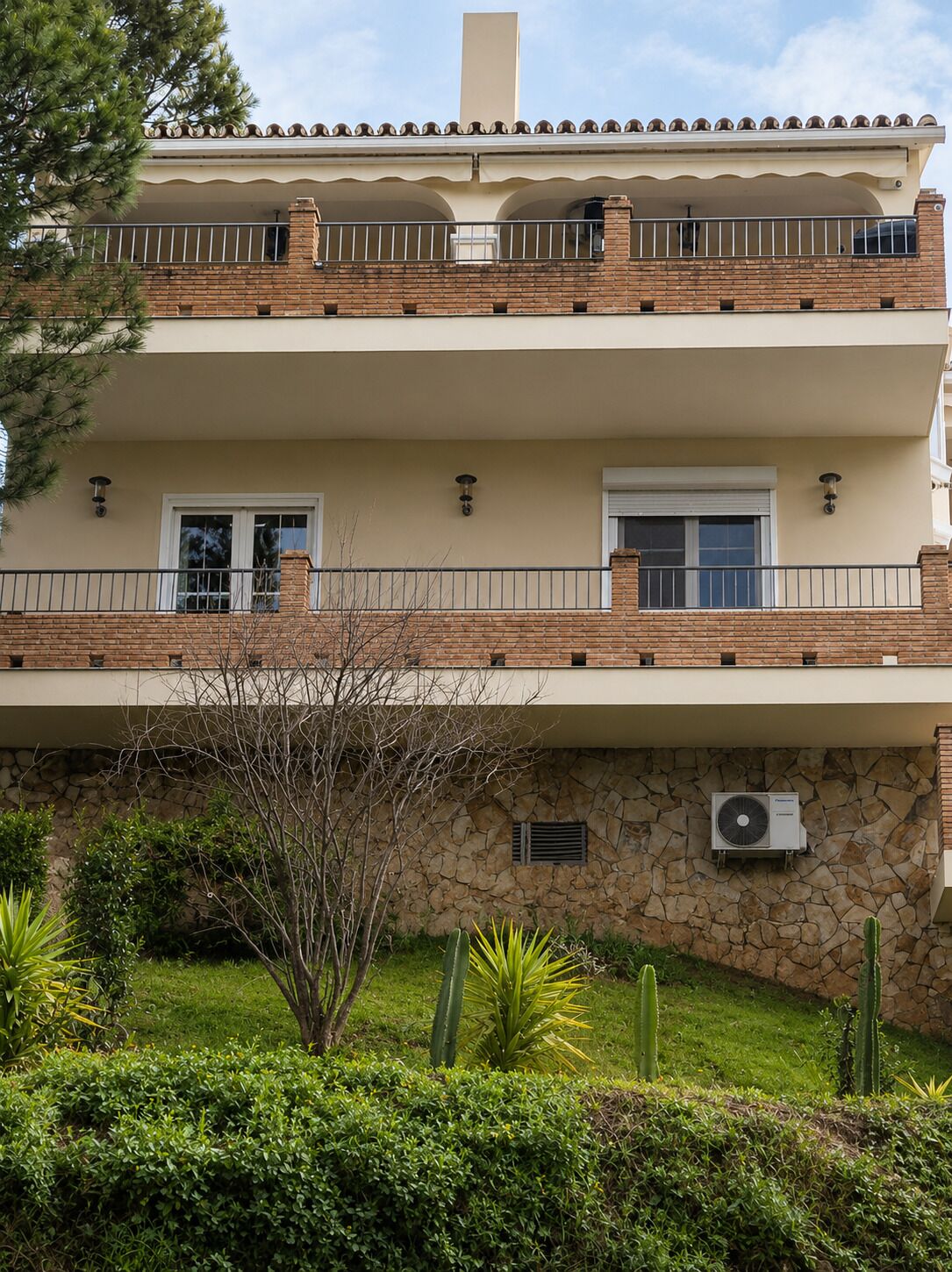 A two-story building with a balcony, stone facade, and an air conditioning unit.