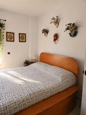 Een slaapkamer met een houten bed, een bed met een patroon erop en decoratieve maskers aan de muur.