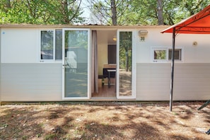 Una casa móvil de una sola planta, pequeña, con entrada por una puerta corrediza de vidrio, un área de cocina adjunta y un patio con mesa y sillas.