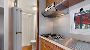 A compact kitchenette with a gas stove, wooden cabinets, and a window with a view of greenery. - Mobile home with air conditioning and 3 shared pools (Bucine)