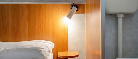 Una habitación de hotel pequeña con cama, una mesita de noche de madera y un inodoro.