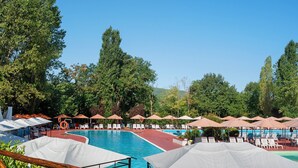 Una piscina amb diverses gandules i ombrelles, envoltada d'arbres.