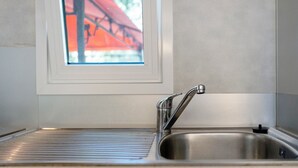 Een keuken met een roestvrijstalen spoelbak, een raam met uitzicht op een rode constructie, en een betegelde spatwand.