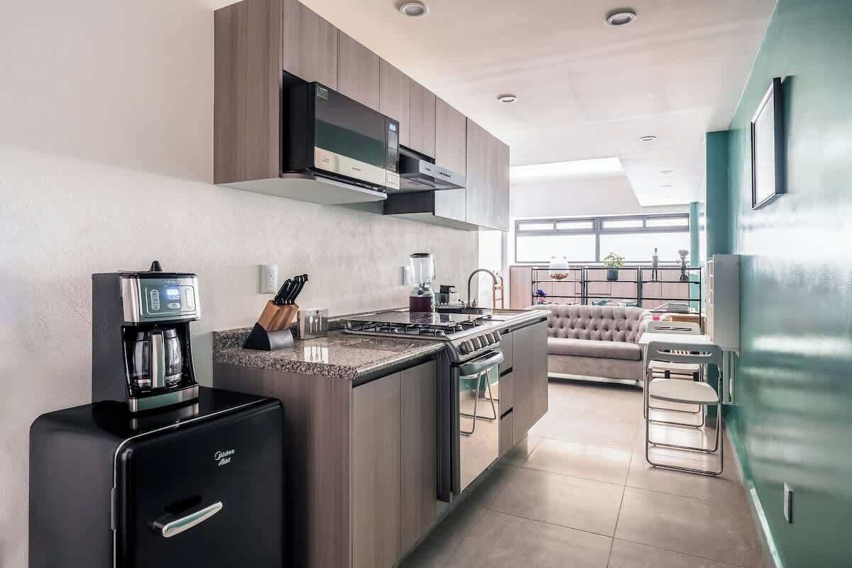 A modern kitchen with a built-in stove, coffee machine, and a compact refrigerator.