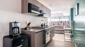 Cuina moderna amb fogó de vitroceràmica, màquina de cafè i frigorífic compacte.