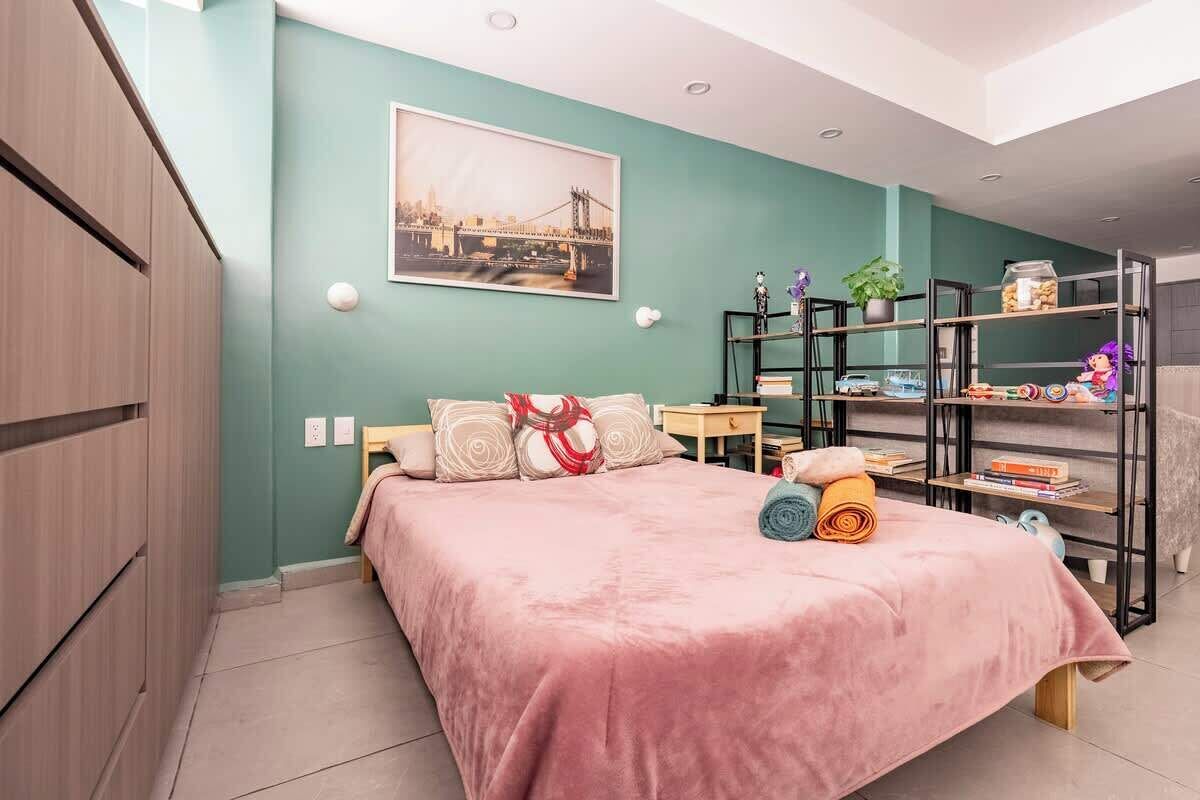 A bedroom with a bed, a nightstand, a bookshelf, and a cityscape painting on the wall.