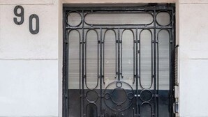 Um portão de metal preto com um desenho decorativo, o número '90' acima e uma placa de metal com 'LARAS'.