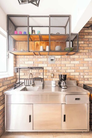 A kitchen with a stainless steel countertop, a coffee maker, and a brick wall. - Cozy and centrally located near Polanco (Mexico City)
