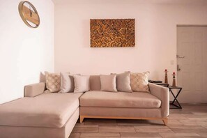 A living room with a beige sectional sofa, a wall clock, and a textured artwork. - Cozy and centrally located near Polanco (Mexico City)