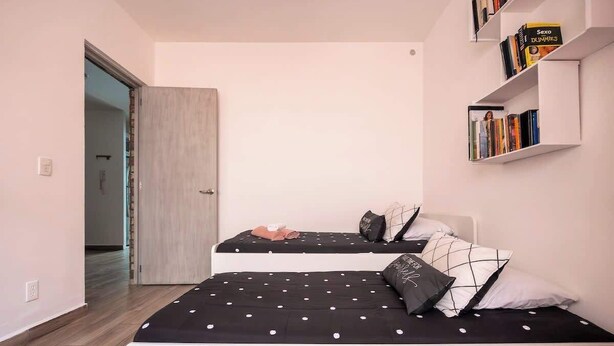 Quarto com duas camas, uma estante de livros e uma porta que dá para outro espaço.