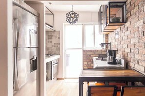 A modern kitchen with a stainless steel refrigerator, a brick wall, and a hanging light fixture. - Cozy and centrally located near Polanco (Mexico City)