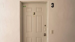 Uma porta branca com o número 3, uma fechadura e um interfone.