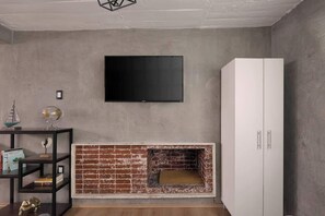 A room with a flat-screen TV mounted on the wall, a white wardrobe, a brick fireplace, and a small table with decorative items. - Nice & Cozy loft near to Reforma (Mexico City)
