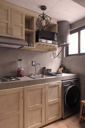Eine kompakte Küche mit Einbau-Mikrowelle, Spüle, Mixer und Waschmaschine.
