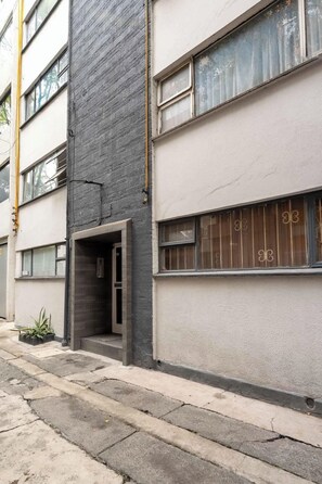 A multi-story building with a grey brick facade, a visible entrance, and a window with a metal grill. - Nice & Cozy loft near to Reforma (Mexico City)