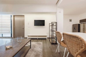 A modern hotel room with a wooden dining table, wicker chairs, a flat-screen TV mounted on the wall, a bench, and a wardrobe. - The Nice & Cozy Urban Green Haven (Ciudad de México)