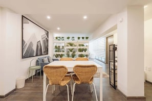 A dining area with a white table, wicker chairs, a cityscape painting, and a plant wall. - The Nice & Cozy Urban Green Haven (Ciudad de México)