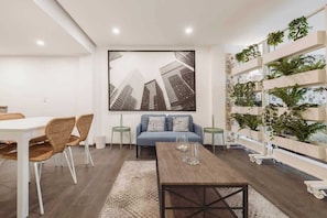 A modern living room with a sofa, dining table, chairs, and a coffee table. There is a large framed picture on the wall and a plant wall on the right. - The Nice & Cozy Urban Green Haven (Ciudad de México)