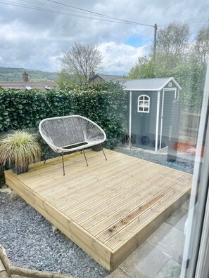 A wooden deck with a white chair, a small shed, and a hedge in a residential setting. - Cosmos Cottage - A colourful homely cottage in Matlock Peak District staycation (Matlock)