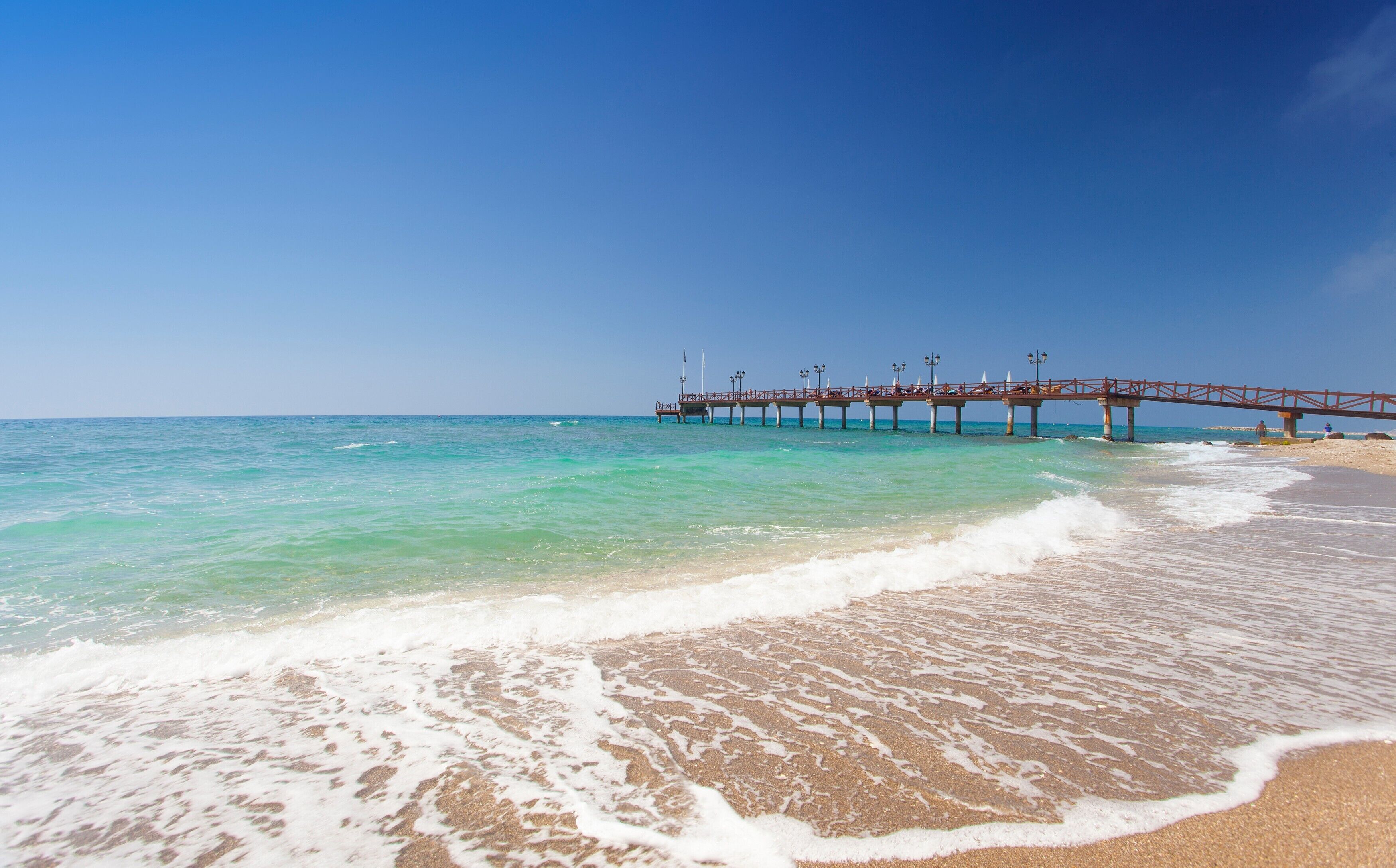 A beach with a pier extending into the ocean, clear skies, and calm waters.