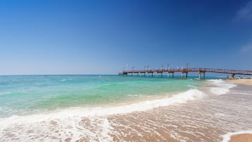 A beach with a pier extending into the ocean, clear skies, and calm waters.