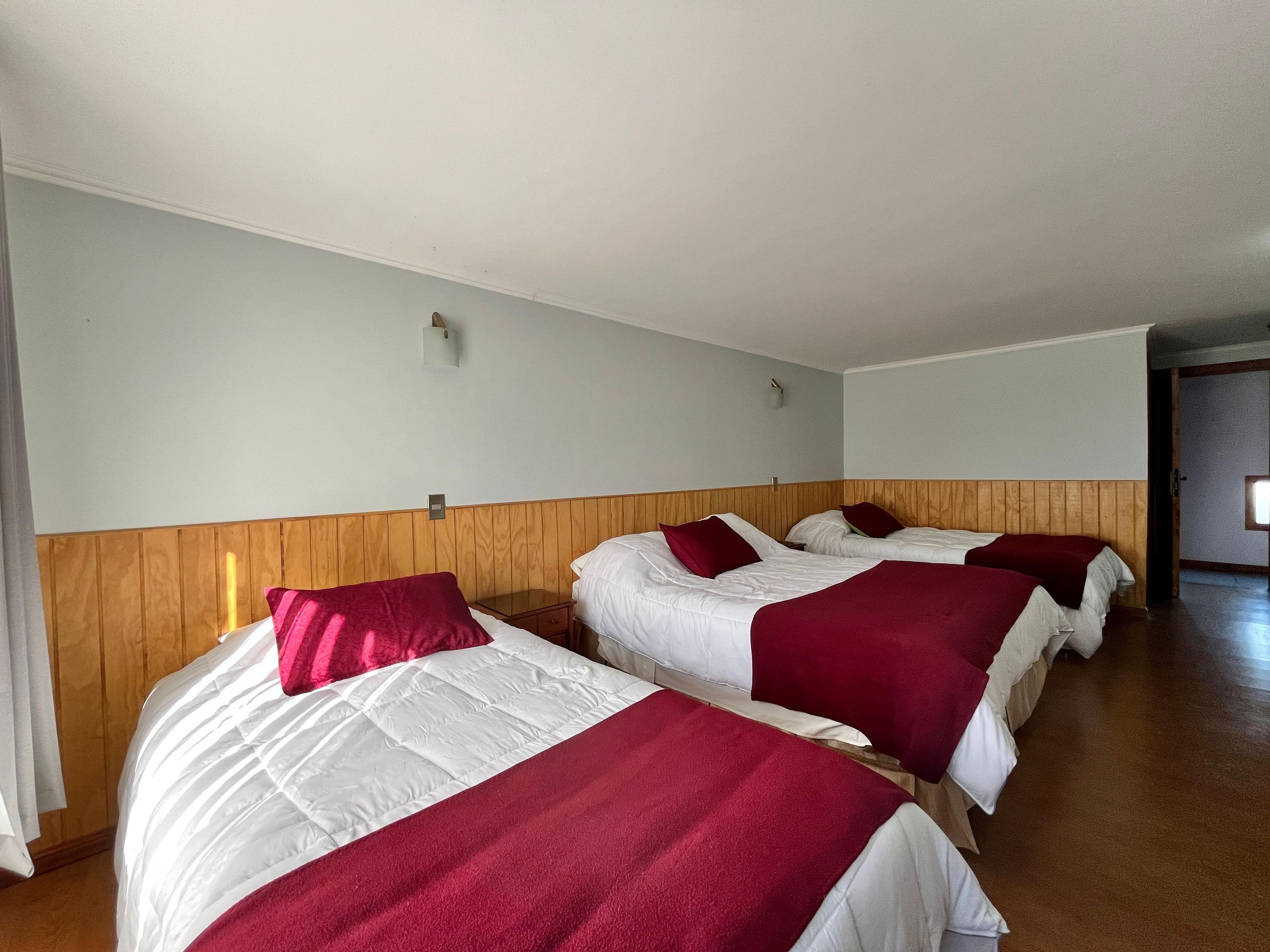 A hotel room with four single beds, wooden headboards, and a light-colored wall.