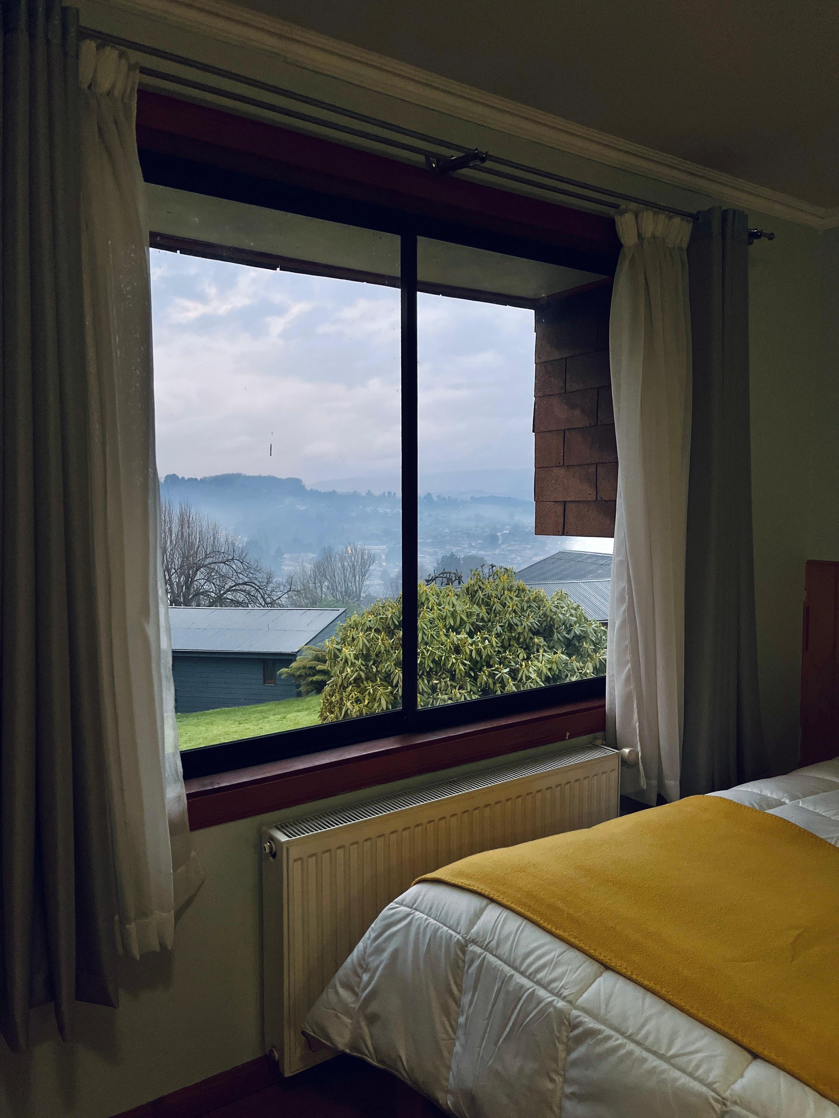 A room with a large window, a radiator, and a bed with a yellow blanket.