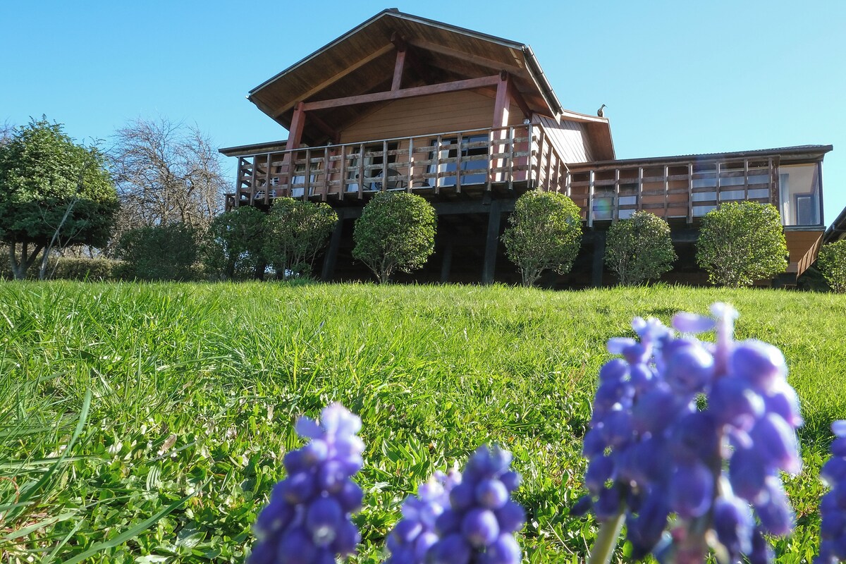 A wooden building with a balcony, surrounded by a grassy field and trees.