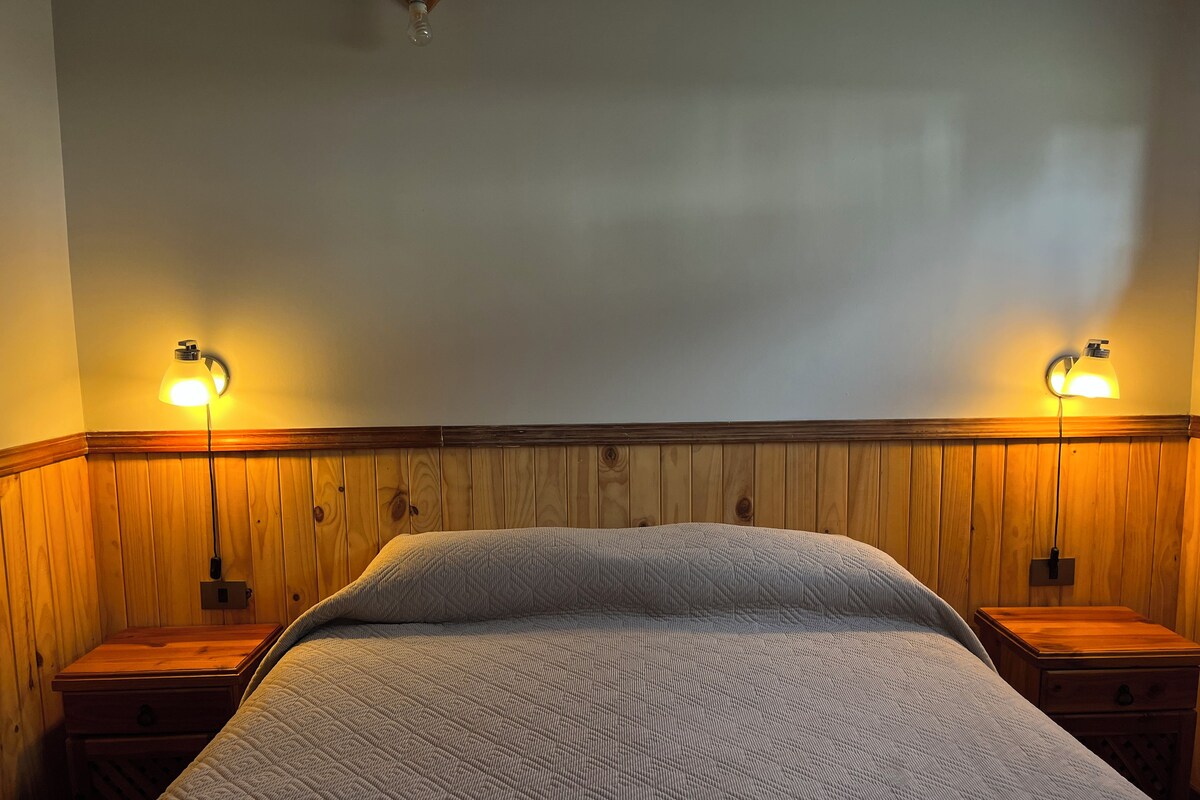 A room with a bed, two bedside tables, and wall-mounted lamps.