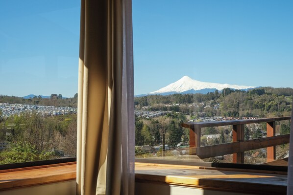 A view of a snow-capped mountain from a window with a wooden railing.
