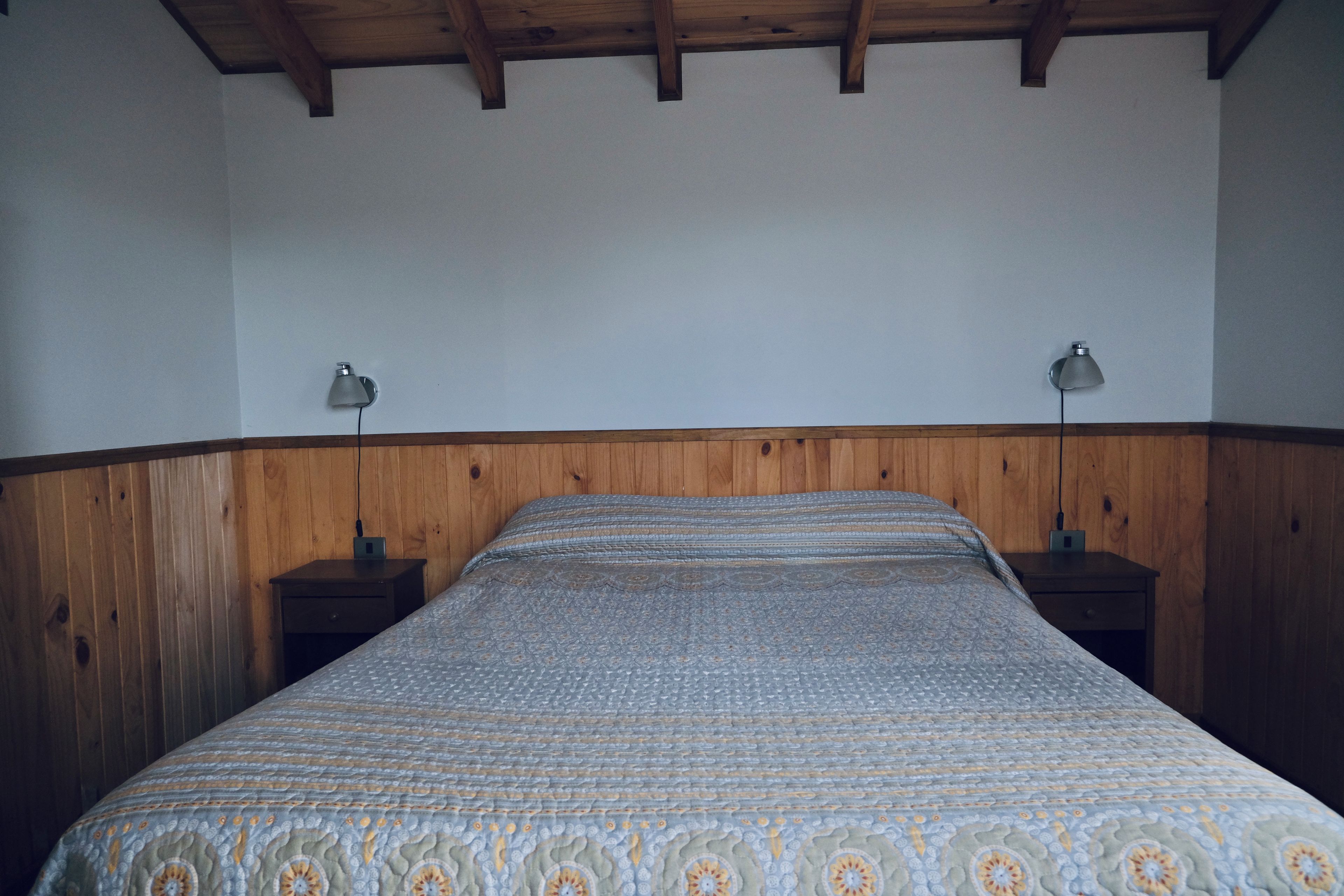 Un dormitorio con cabecera de madera, colcha estampada y dos lámparas de noche.
