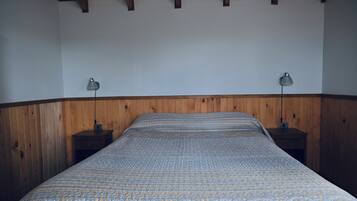 Un dormitorio con cabecera de madera, colcha estampada y dos lámparas de noche.