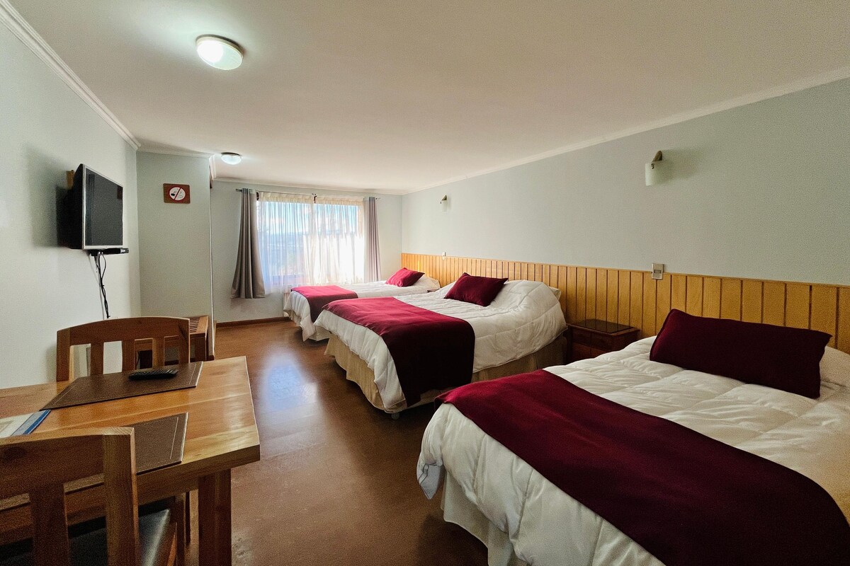 A hotel room with three beds, a desk, and a television.